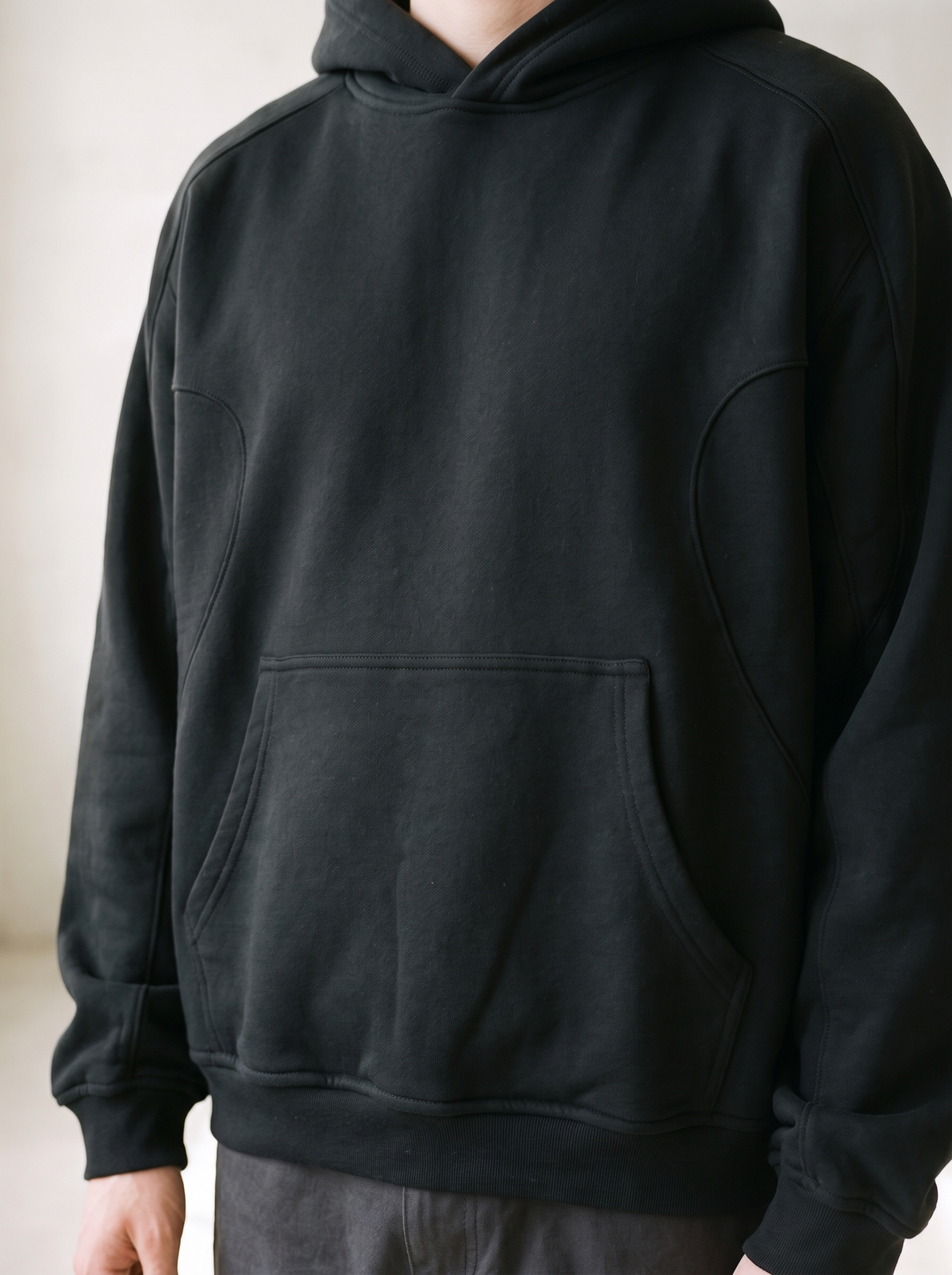 Plain black heavyweight hoodie worn by a model, close up on the kangaroo pocket