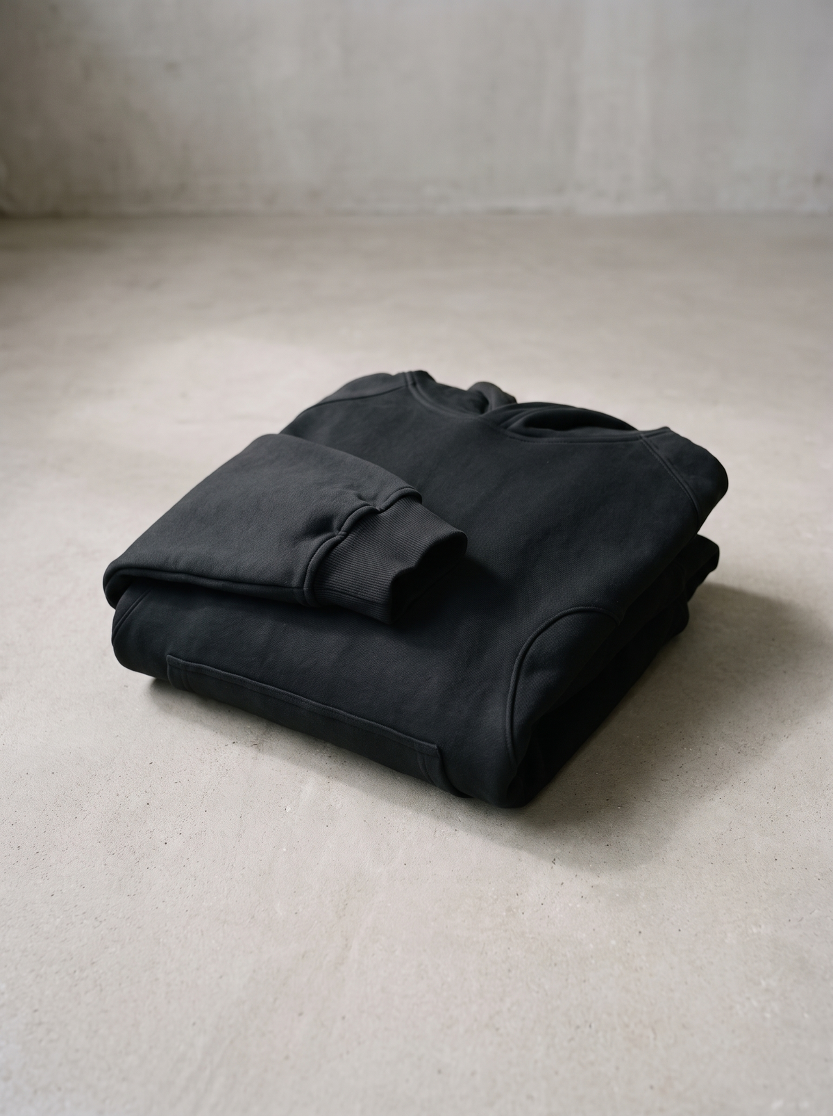 Plain black heavyweight hoodie folded on a smooth concrete floor