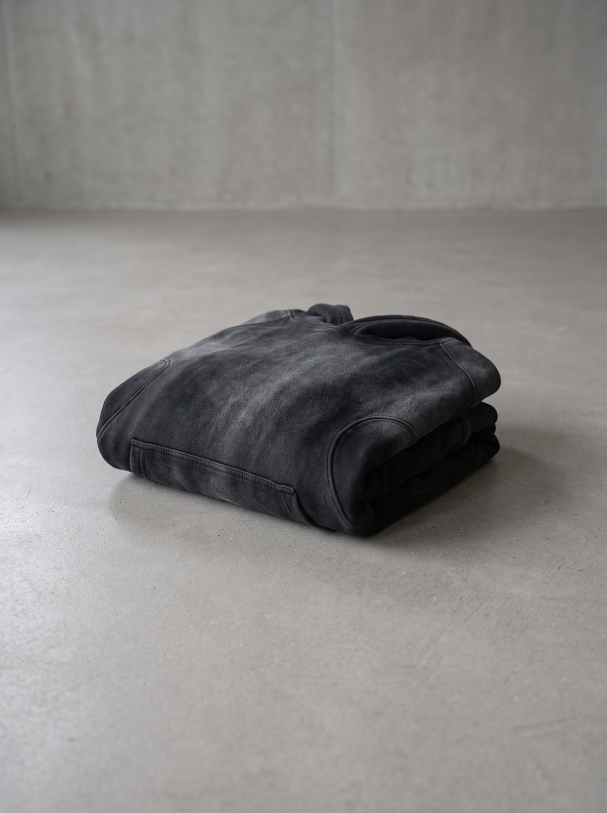 Sunfaded monochrome hoodie folded on a smooth concrete floor