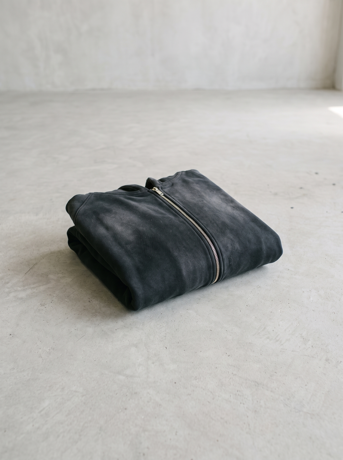 Sunfaded black zip up hoodie folded on a smooth concrete floor