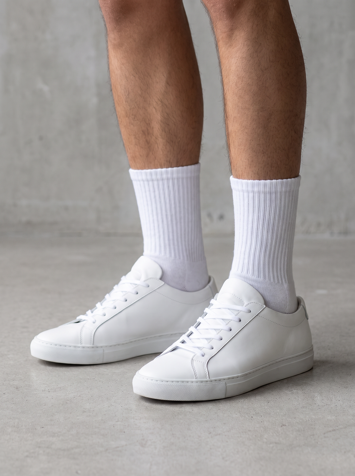 White sports crew socks worn with sneakers on a concrete floor